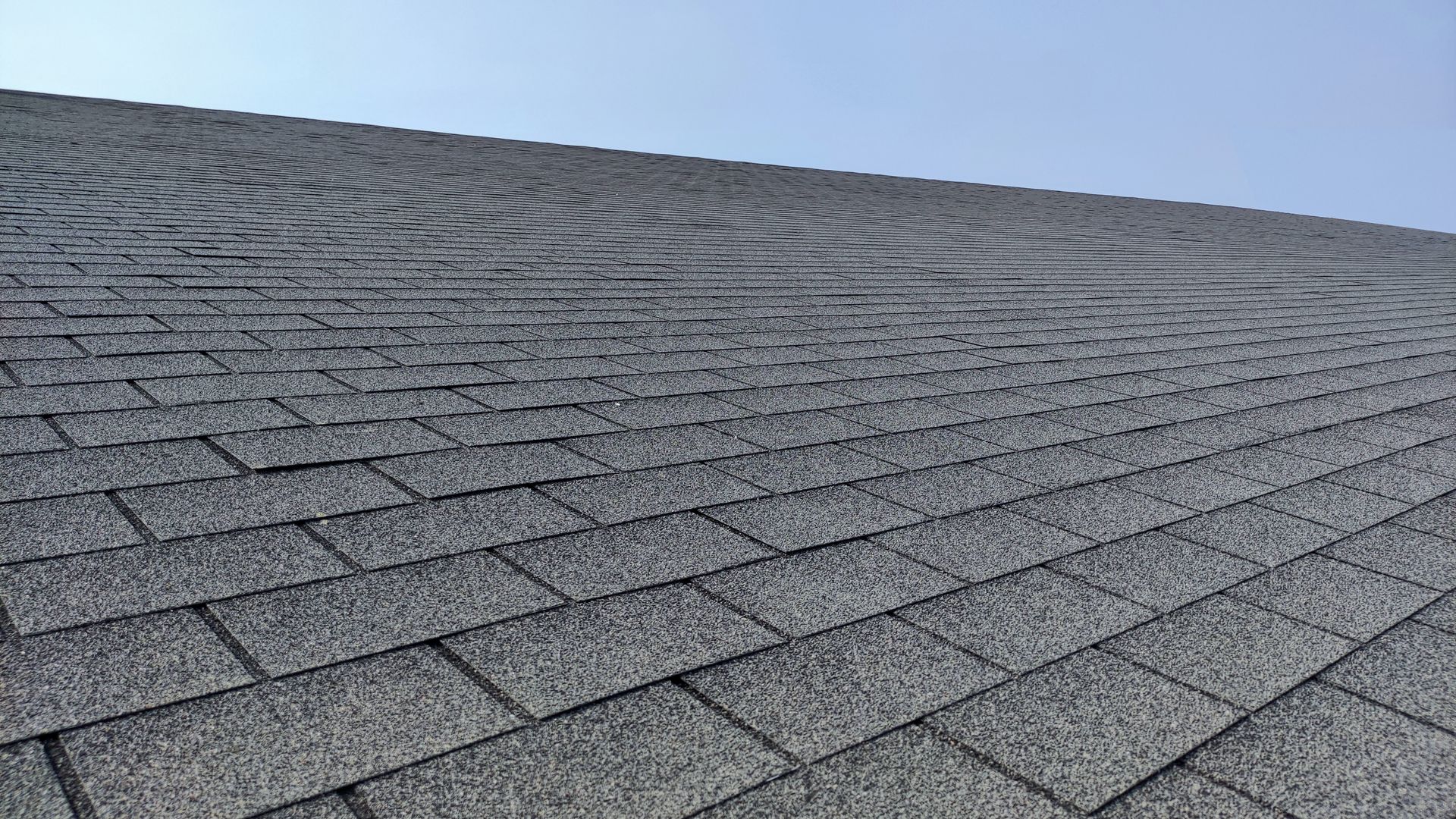 A close up of a roof with shingles against a blue sky.