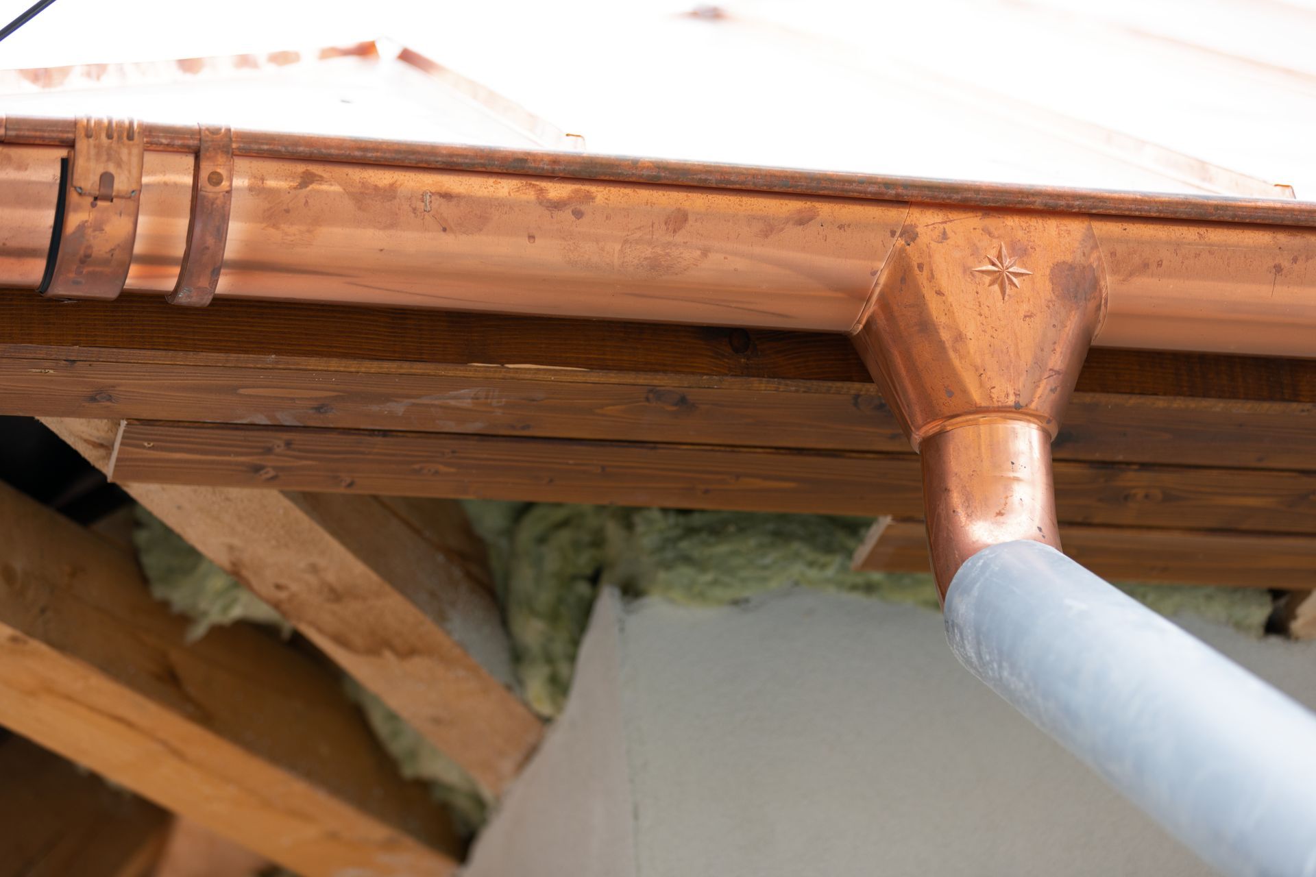 A close up of a copper gutter on a wooden roof.