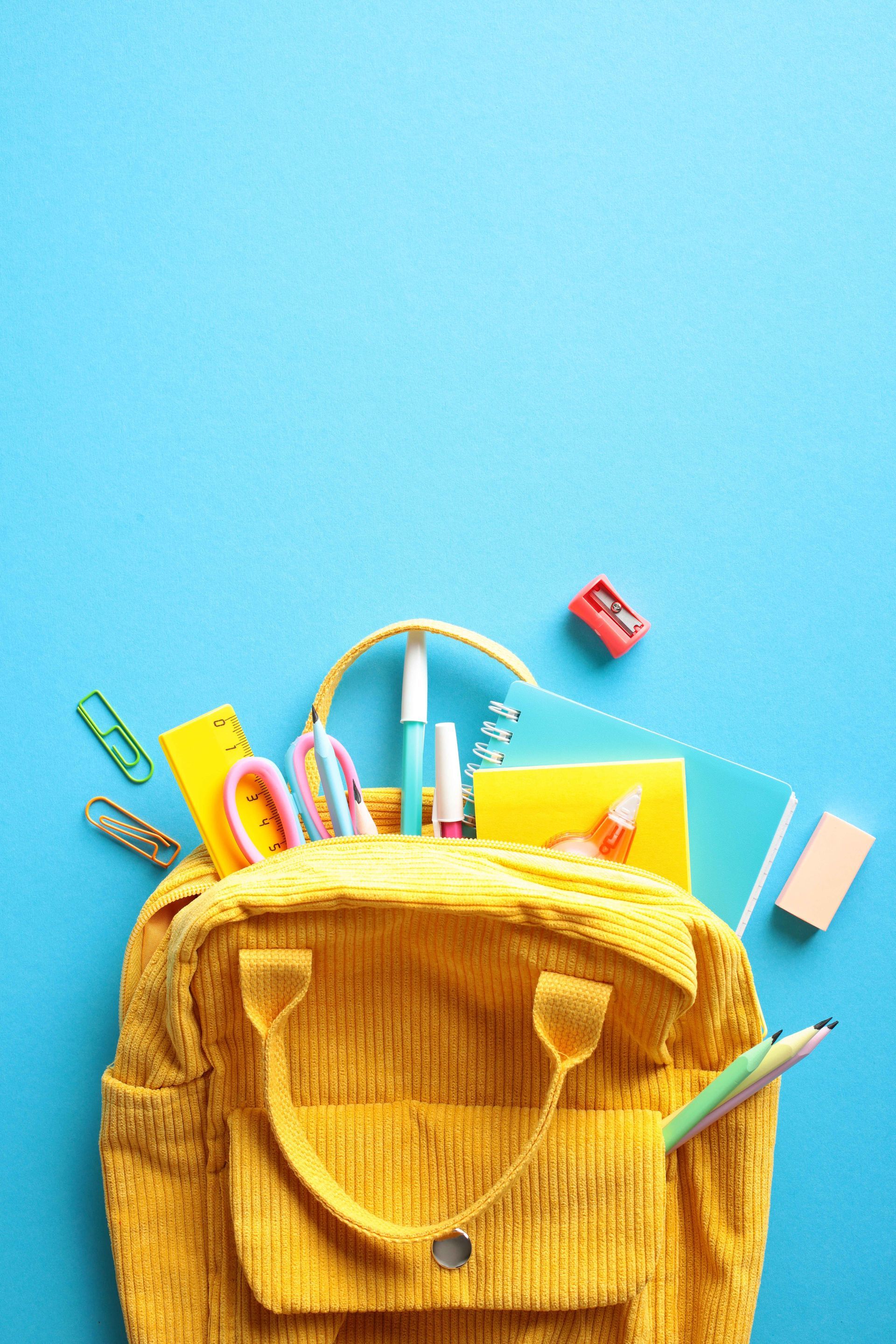 A yellow backpack filled with school supplies on a blue background.