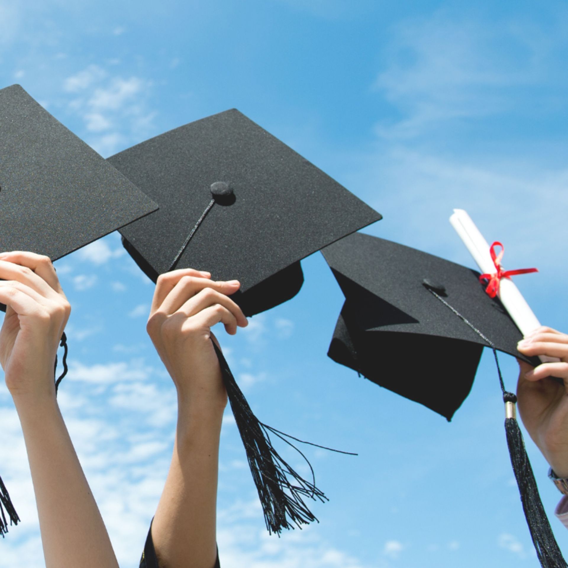 A group of graduates are holding their caps and diplomas in the air