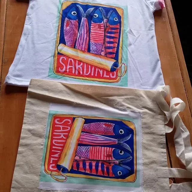 Camiseta blanca y bolso tote color tostado con diseño de lata de sardinas en azul, rojo, rosa y amarillo.
