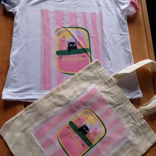 Camisa blanca y bolsa de lona con gráfico rosa y amarillo de un gato negro en un frasco.