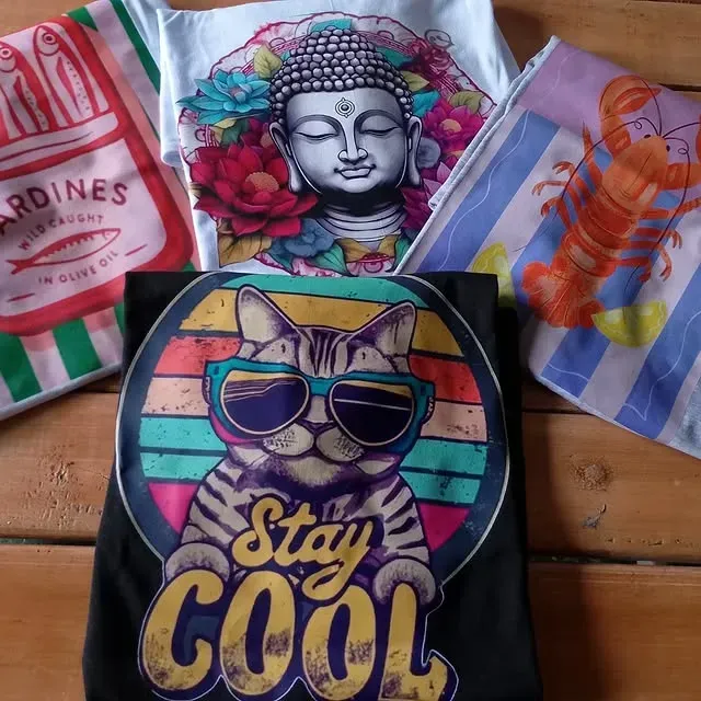 Cinco camisetas coloridas, varios diseños: sardinas, buda, langosta, rayas de playa, gato con gafas de sol.