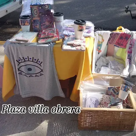 Una mesa de vendedor en la Plaza Villa Obrera, exhibiendo camisetas, tazas y otros artículos.