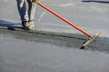 A man is using a rake to spread asphalt on the ground