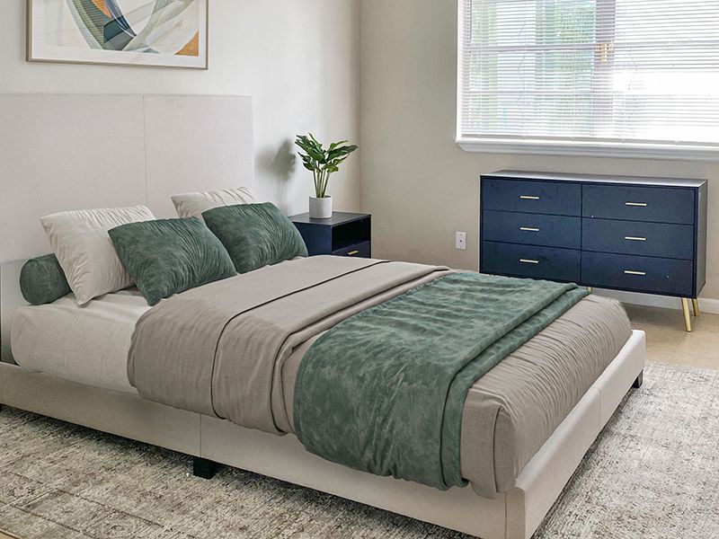 Bedroom with a bed, dresser, and nightstand in neutral tones with green accents.