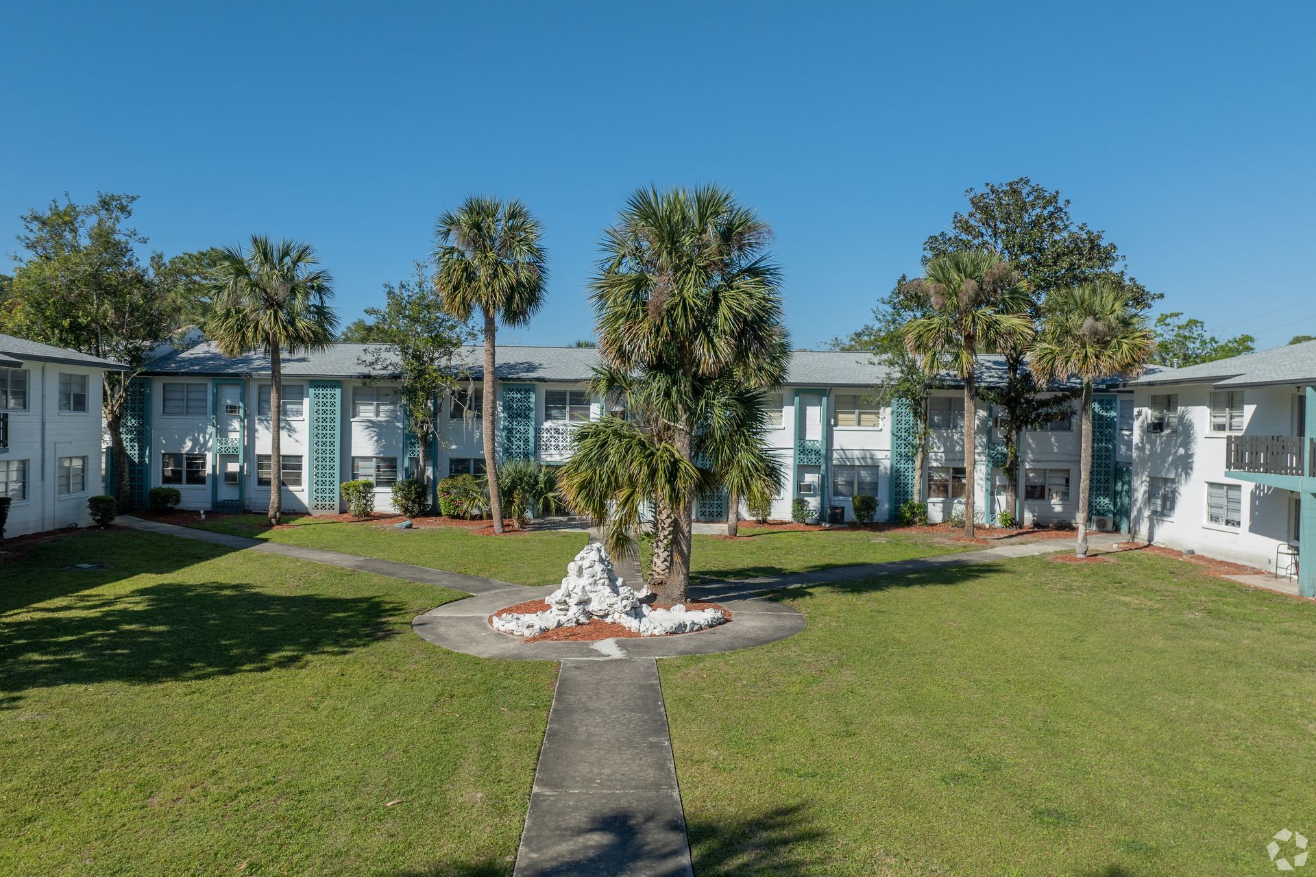 Apartment complex with a central courtyard, surrounded by palm trees and green grass on a sunny day at Caroline Village in Jacksonville, FL.