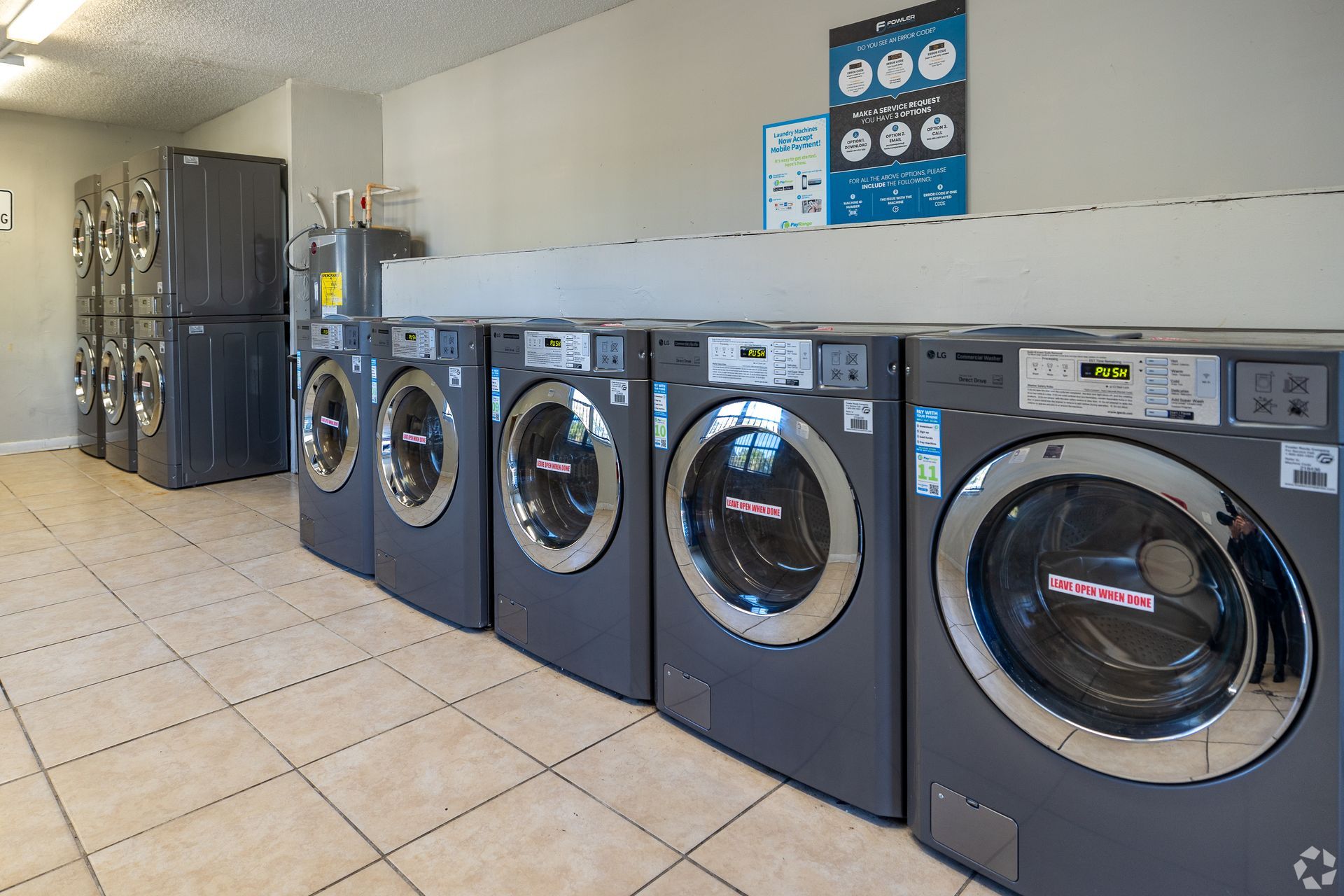 Row of washing machines in a laundry room, with stacked dryers and information signs.