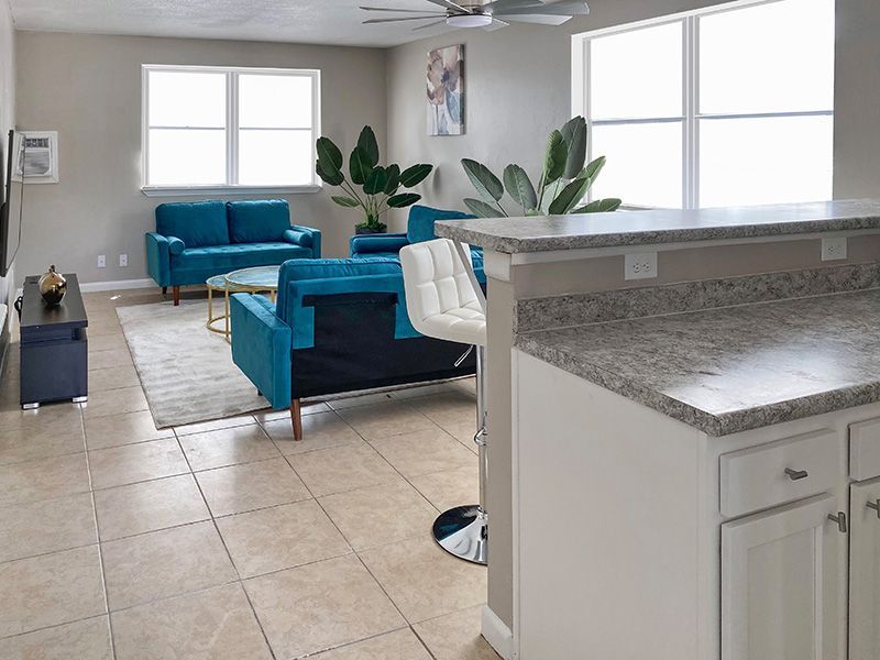 Living room with blue sofas, large windows, and a white kitchen counter.