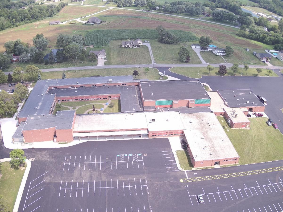 Aerial view of a school campus with parking lots, buildings, and grassy fields beyond.