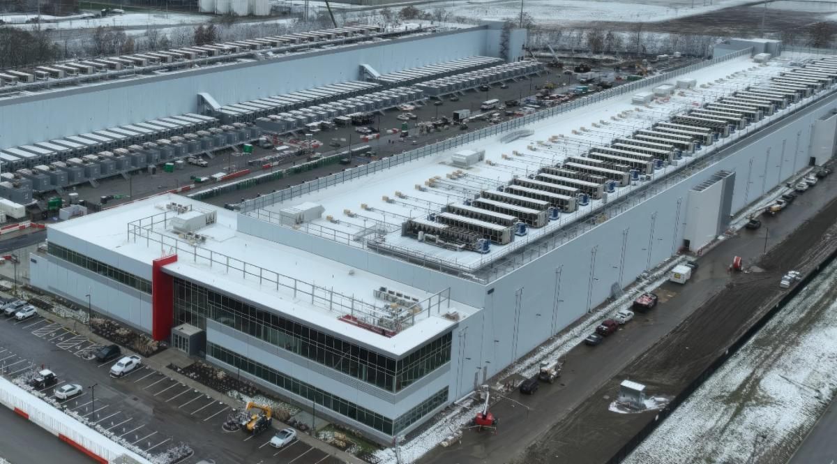 Industrial warehouse with rooftop equipment and parked cars beside a road
