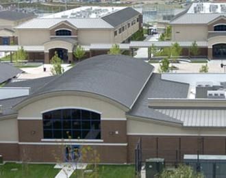 Multi-building school complex with arched roof, tan and brown walls, and large windows.