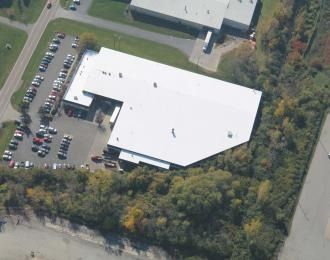 Aerial view of a white-roofed commercial building with a parking lot and surrounding trees.