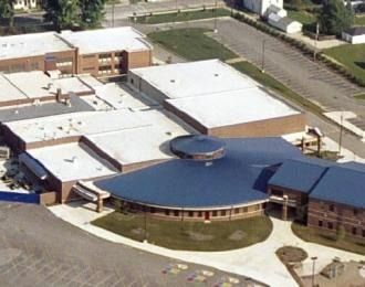 Aerial view of a school building with a blue, circular entrance, flat white roofs, and brick exterior.