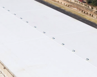 White commercial roof with metal fasteners, near asphalt road and landscaping.