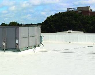 Rooftop with white surface, HVAC unit, and distant building on a hill under a partly cloudy sky.