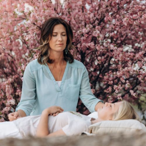 Woman giving healing session outdoors; pink blossoms in the background.