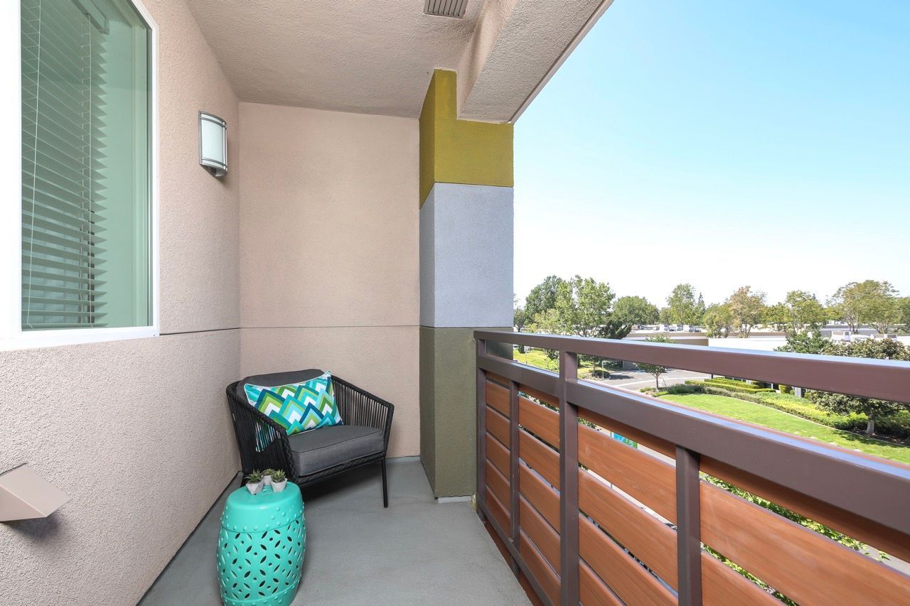 Apartment balcony with a chair, teal stool, and a view of the courtyard.