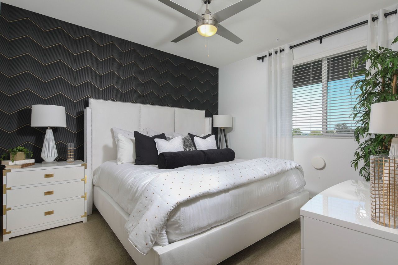 Modern bedroom with a white upholstered bed, matching nightstands, and a large window.