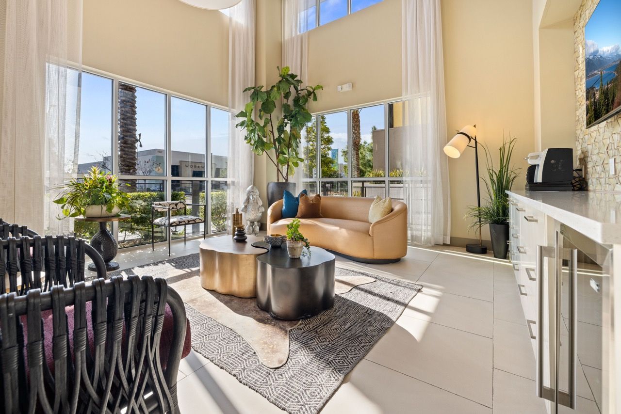 Bright modern living area with tall windows, a tan sofa, and greenery.