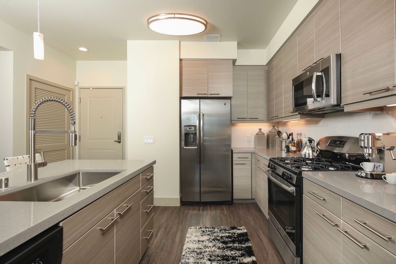 Modern apartment kitchen with an island sink, stainless steel appliances, and light wood cabinets.