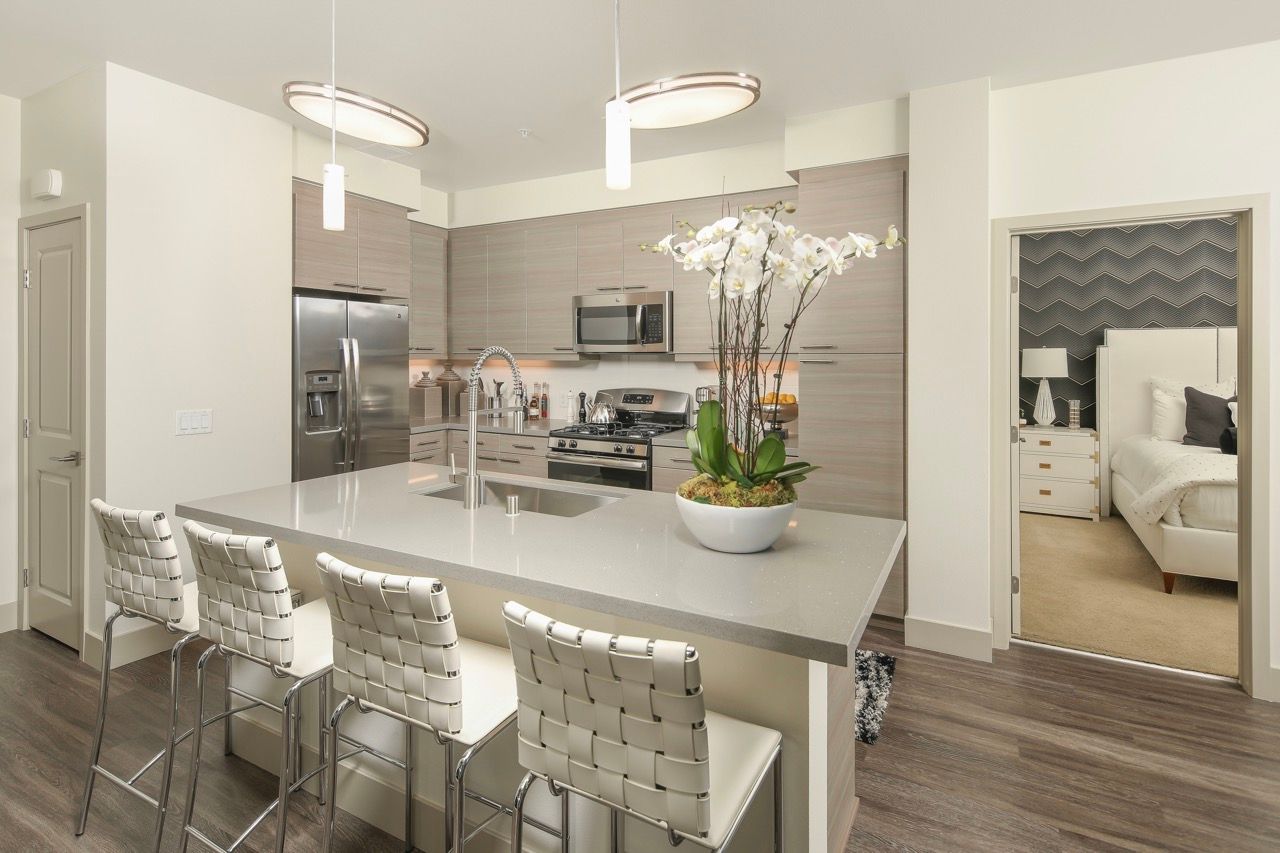 Modern kitchen with a large island, stainless steel appliances, and a doorway to a bedroom.