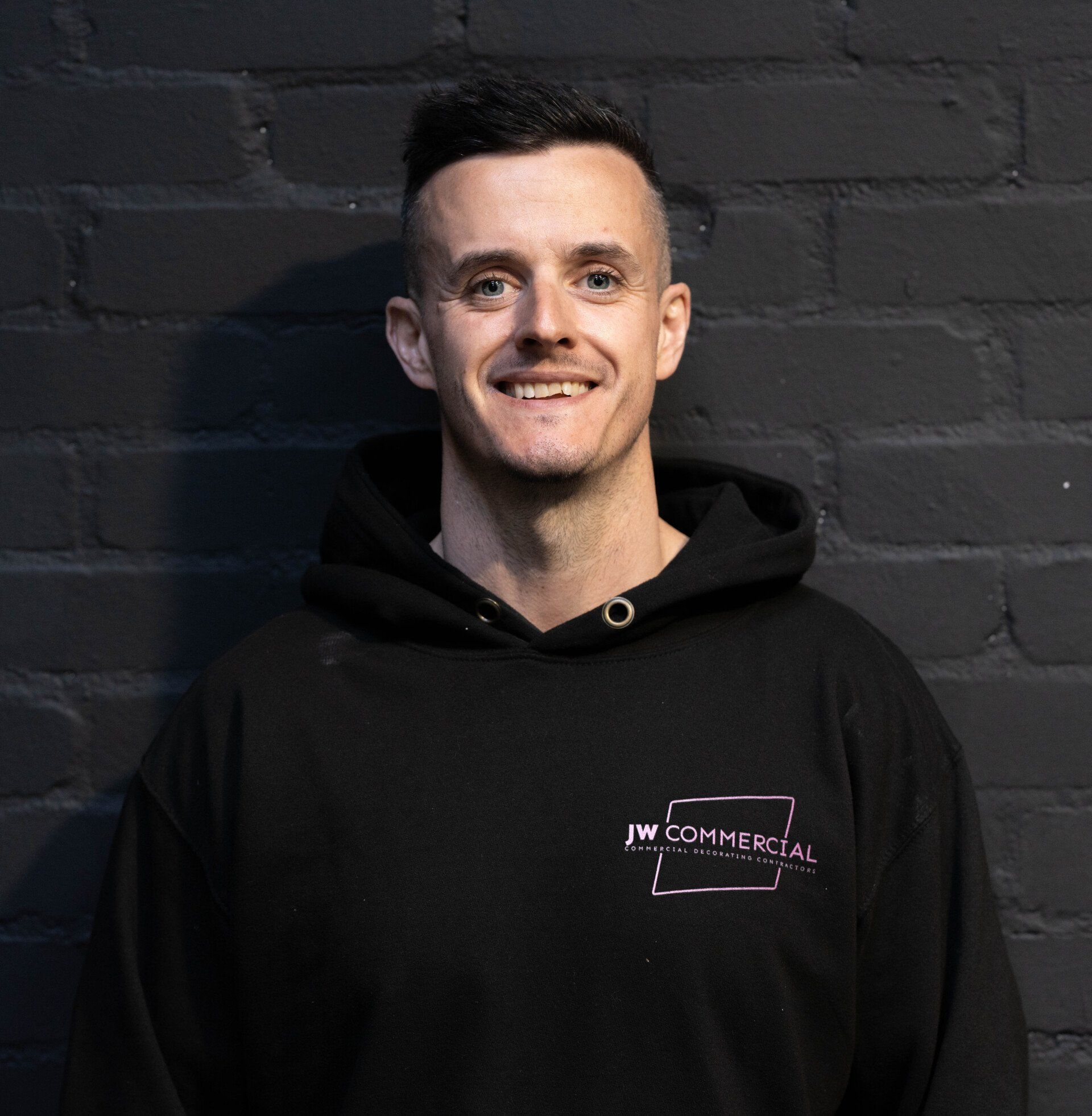 Olly 
smiling, wearing a black hoodie with 