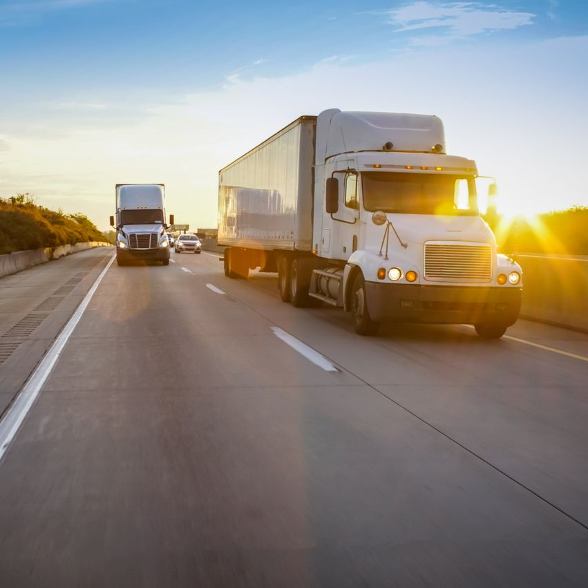 Dos camiones articulados circulando por una autopista al atardecer.