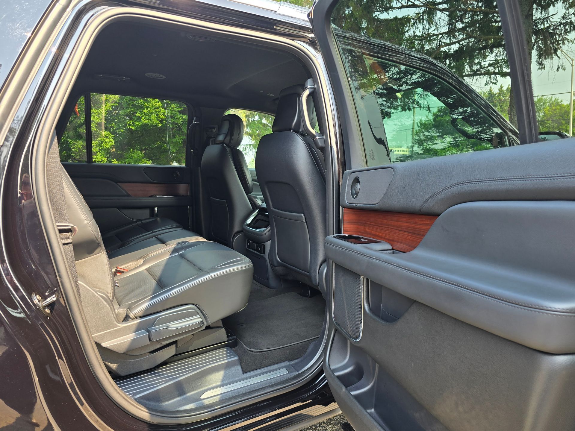 Open black SUV interior with black leather seats, wood trim, and door open.