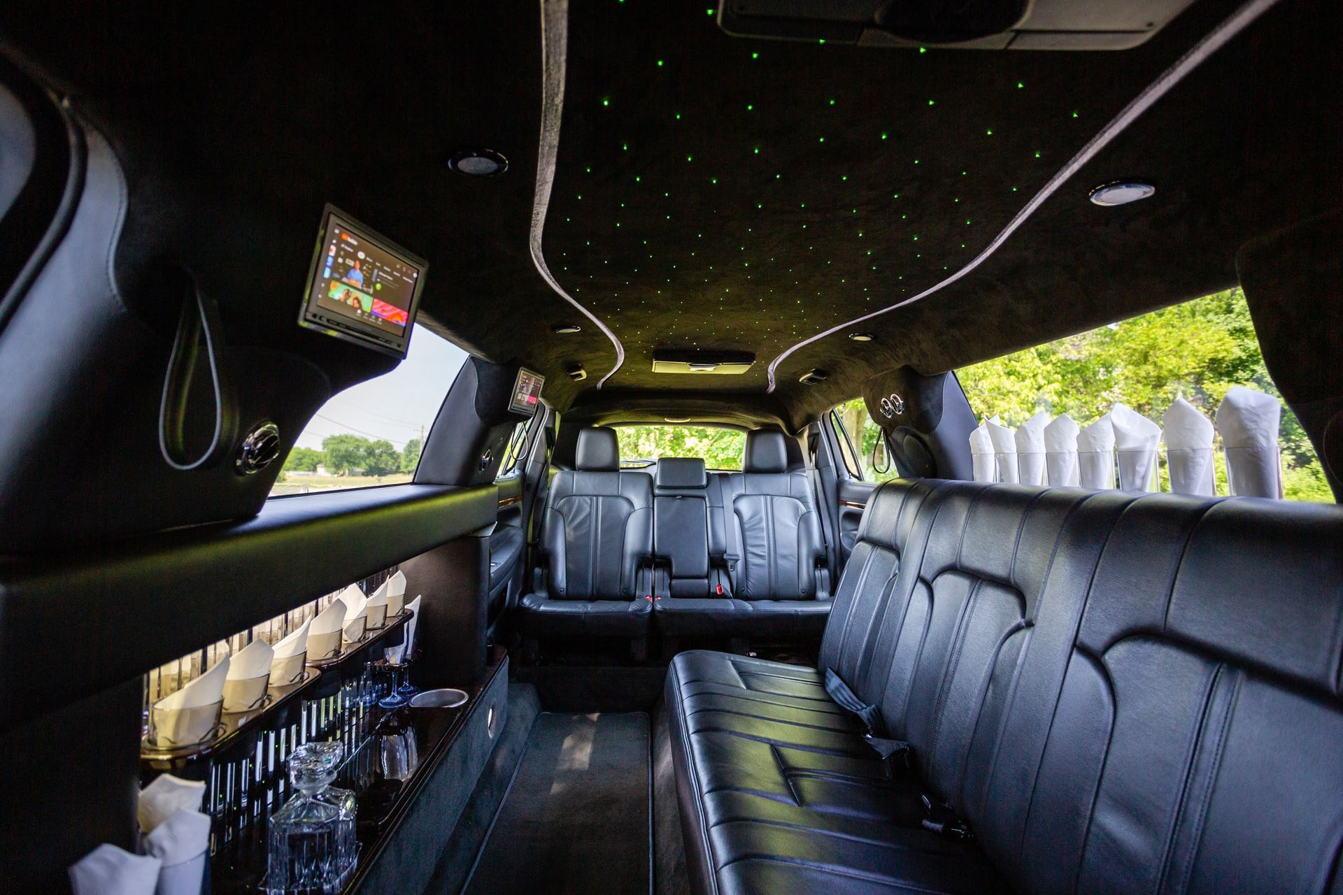 Interior of a black limousine with black leather seating, bar, and starlit ceiling; a rear view.