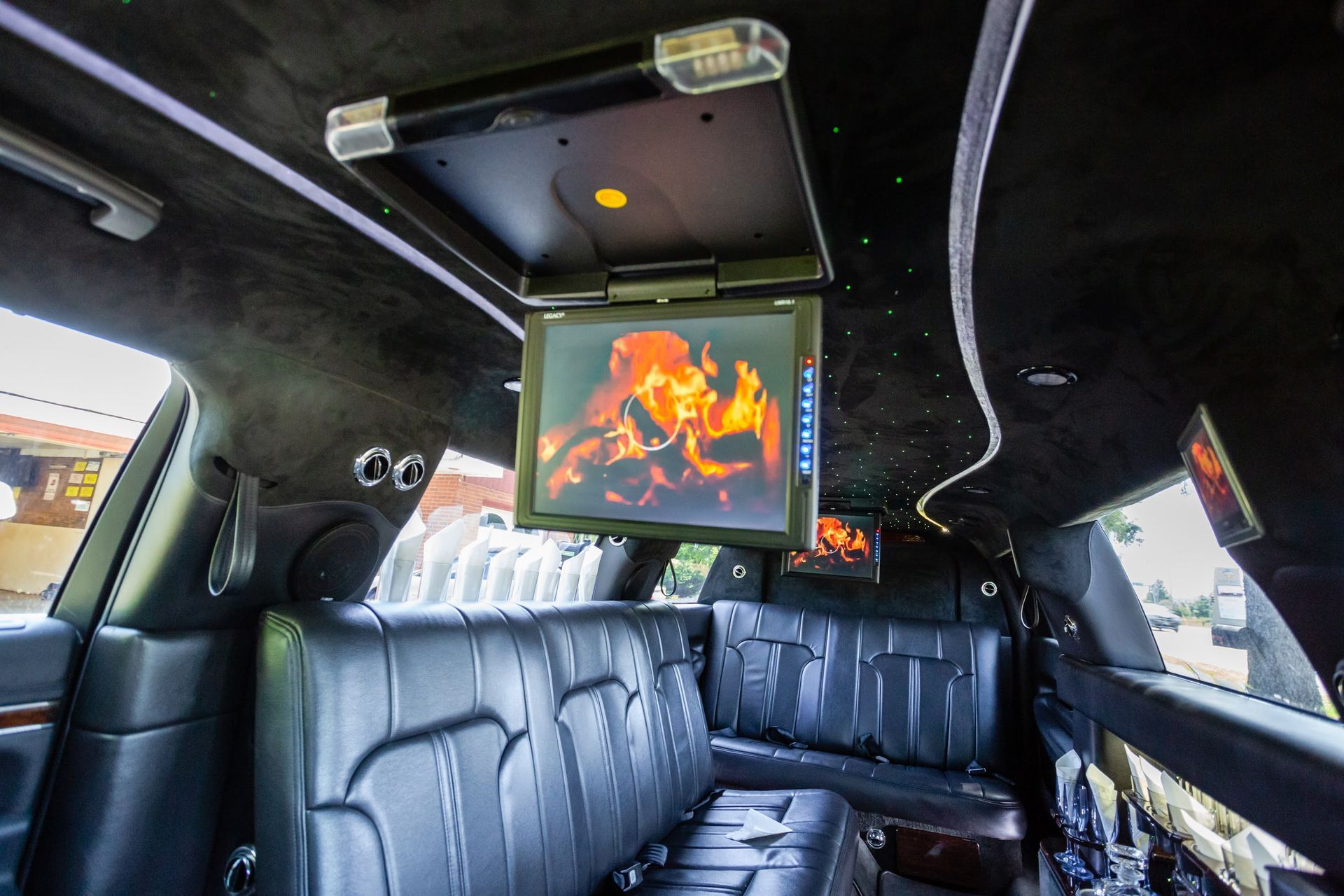 Inside of a black limousine, showing black leather seating and screens displaying a fire.