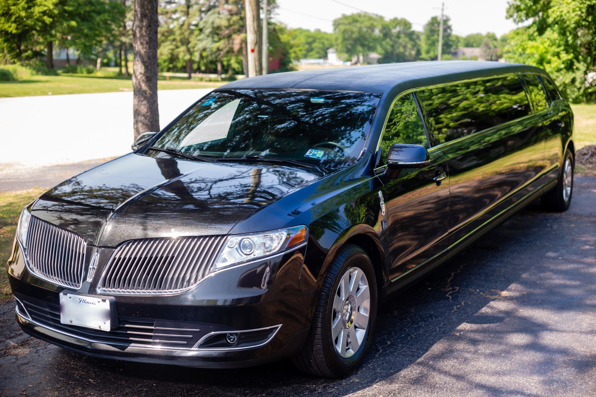 Black Lincoln limousine parked on a paved surface with green grass and trees in the background.