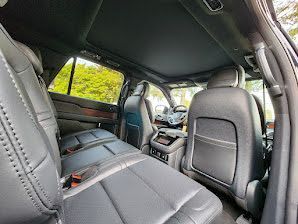 Black leather interior of a large SUV, including back seats, dashboard, and a sunroof.