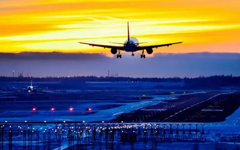 An airplane is taking off from an airport runway at sunset.