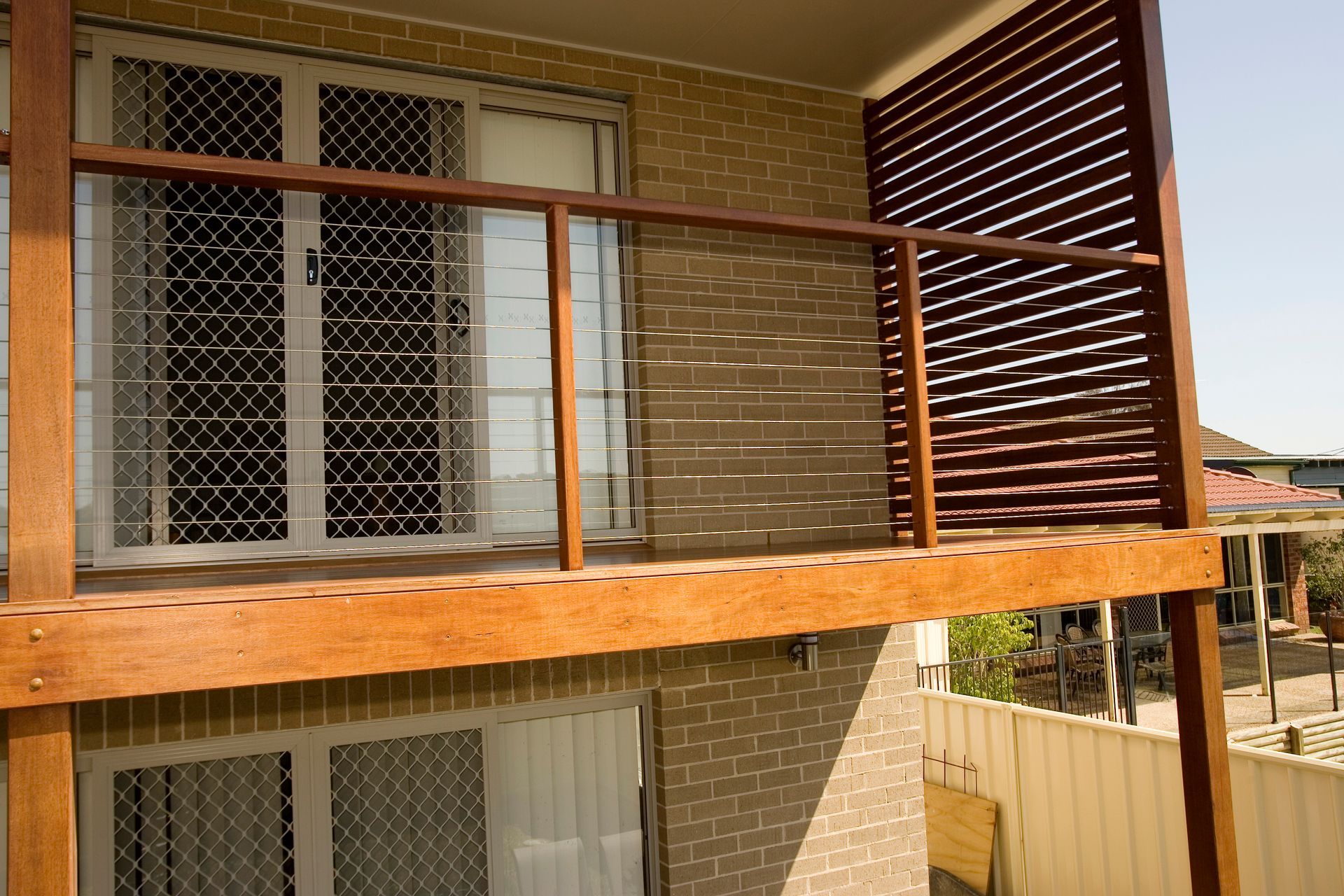 Wooden balcony with brick wall and security screens on windows.