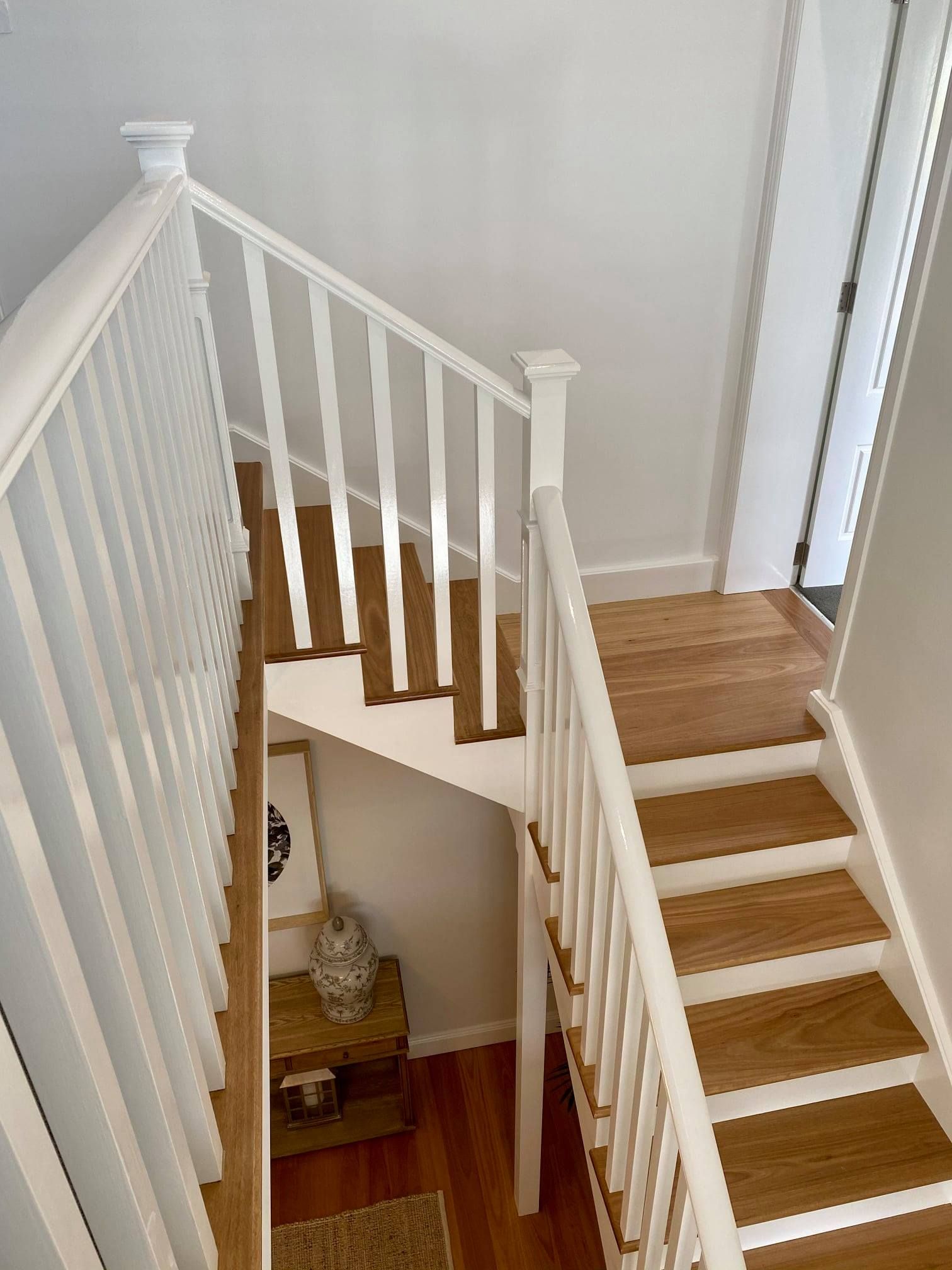 White stairwell with wooden steps. A railing runs along the stairs.