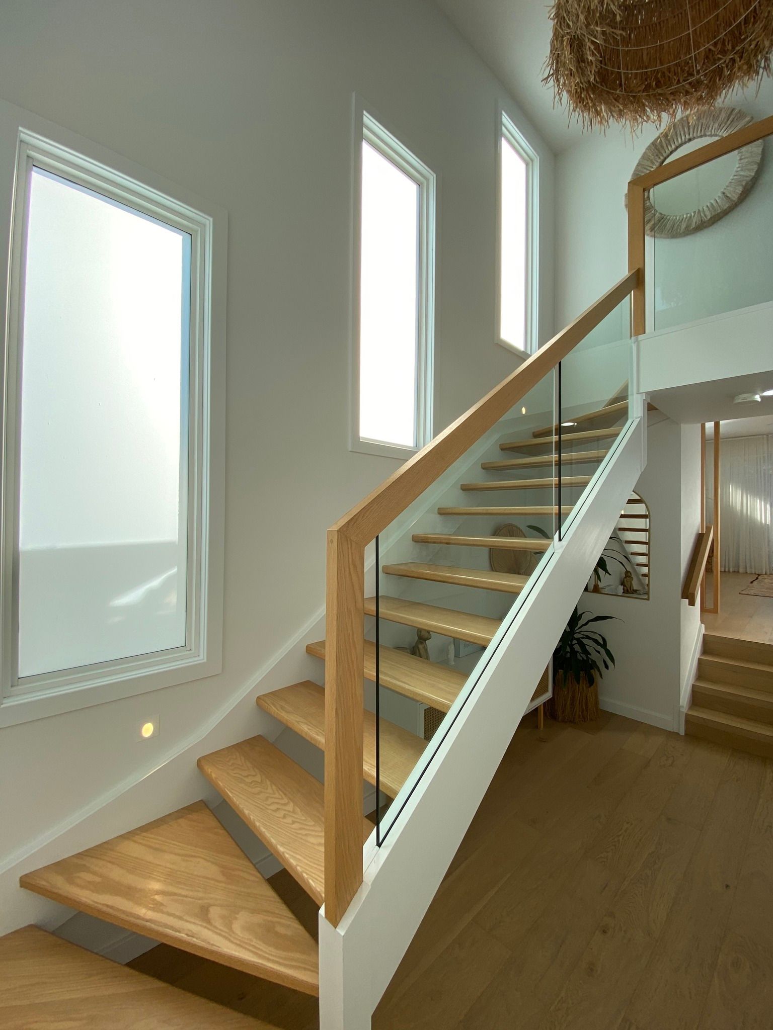 Wooden staircase with glass railing and natural light from windows.