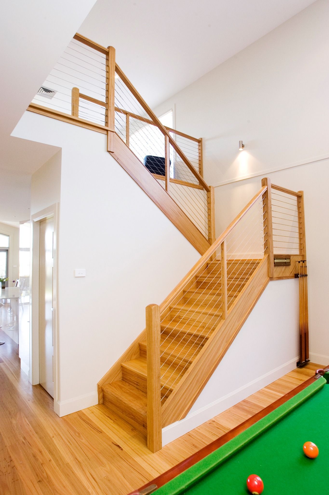 Wooden staircase with cable railings next to a pool table, light-filled interior.