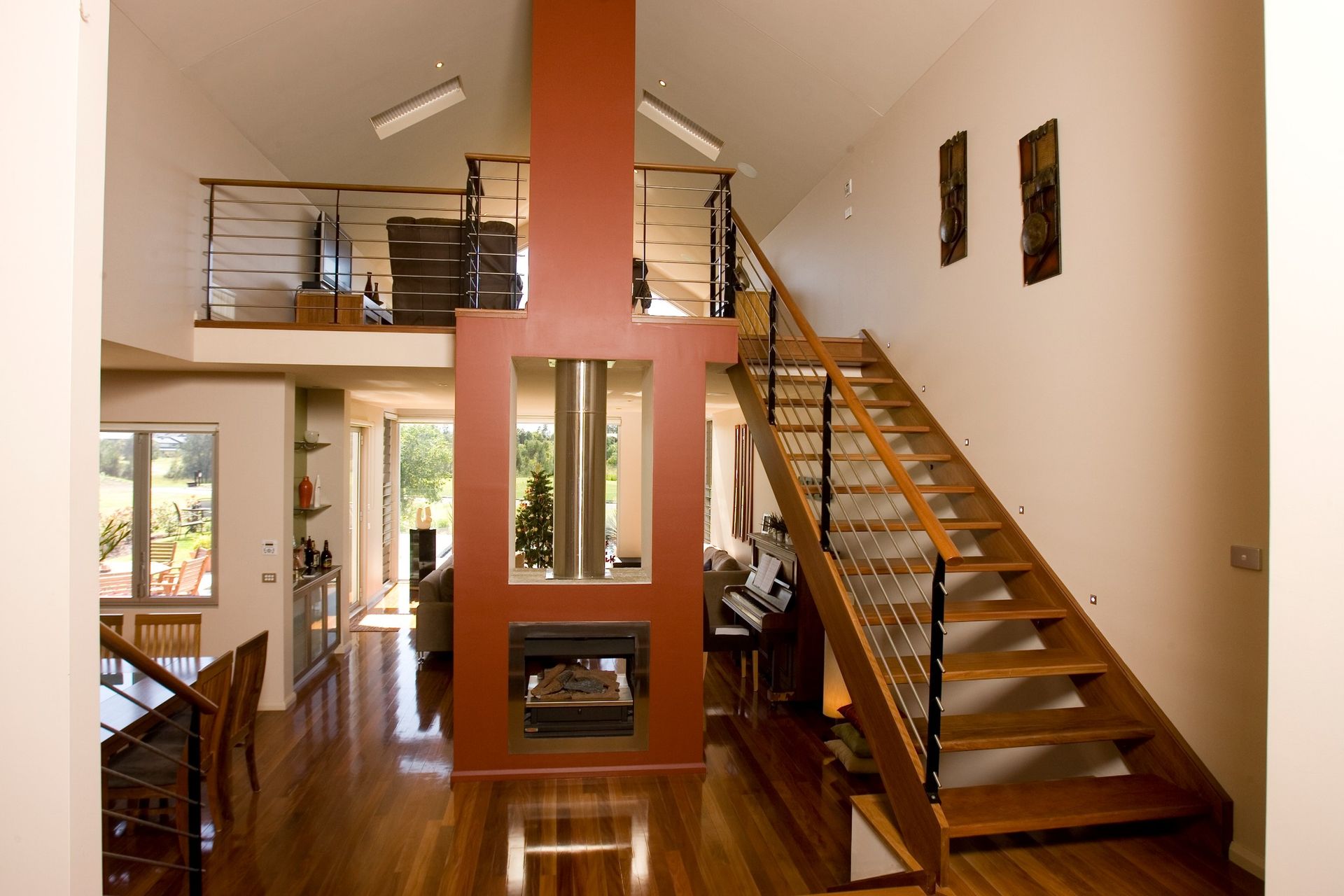 Open-concept living space with wood staircase, fireplace, and loft. Red accent wall, wood floors, and white walls.