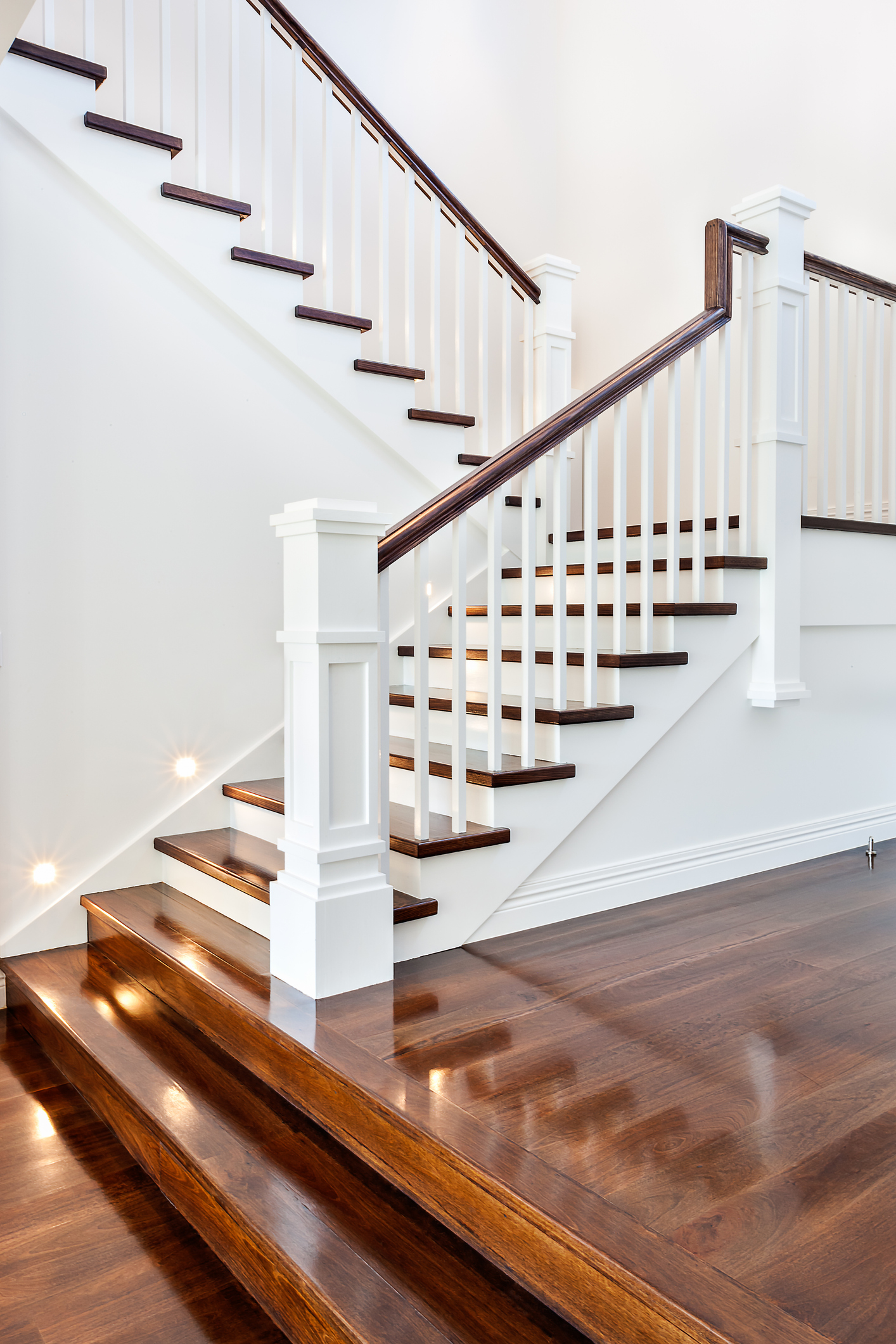 Sleek stairs with glossy wooden steps set against pristine white walls in a luxury home.