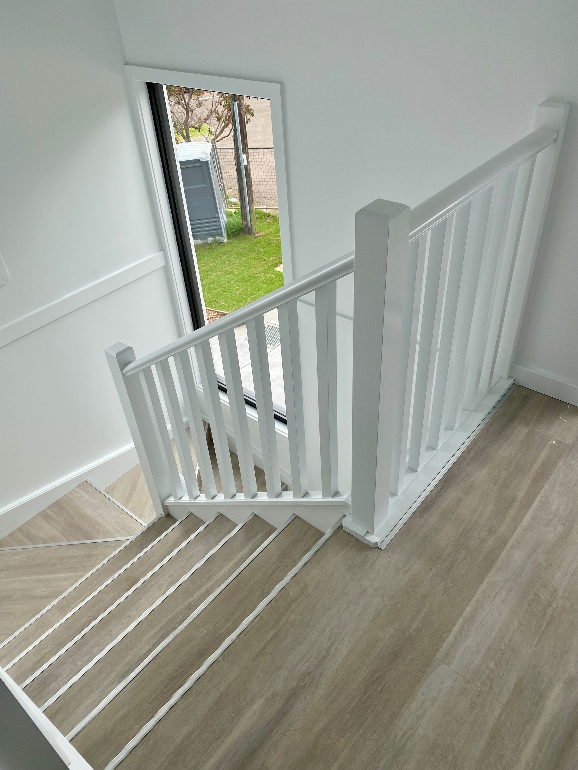 White staircase with railing, leading down towards a window with a grassy yard.