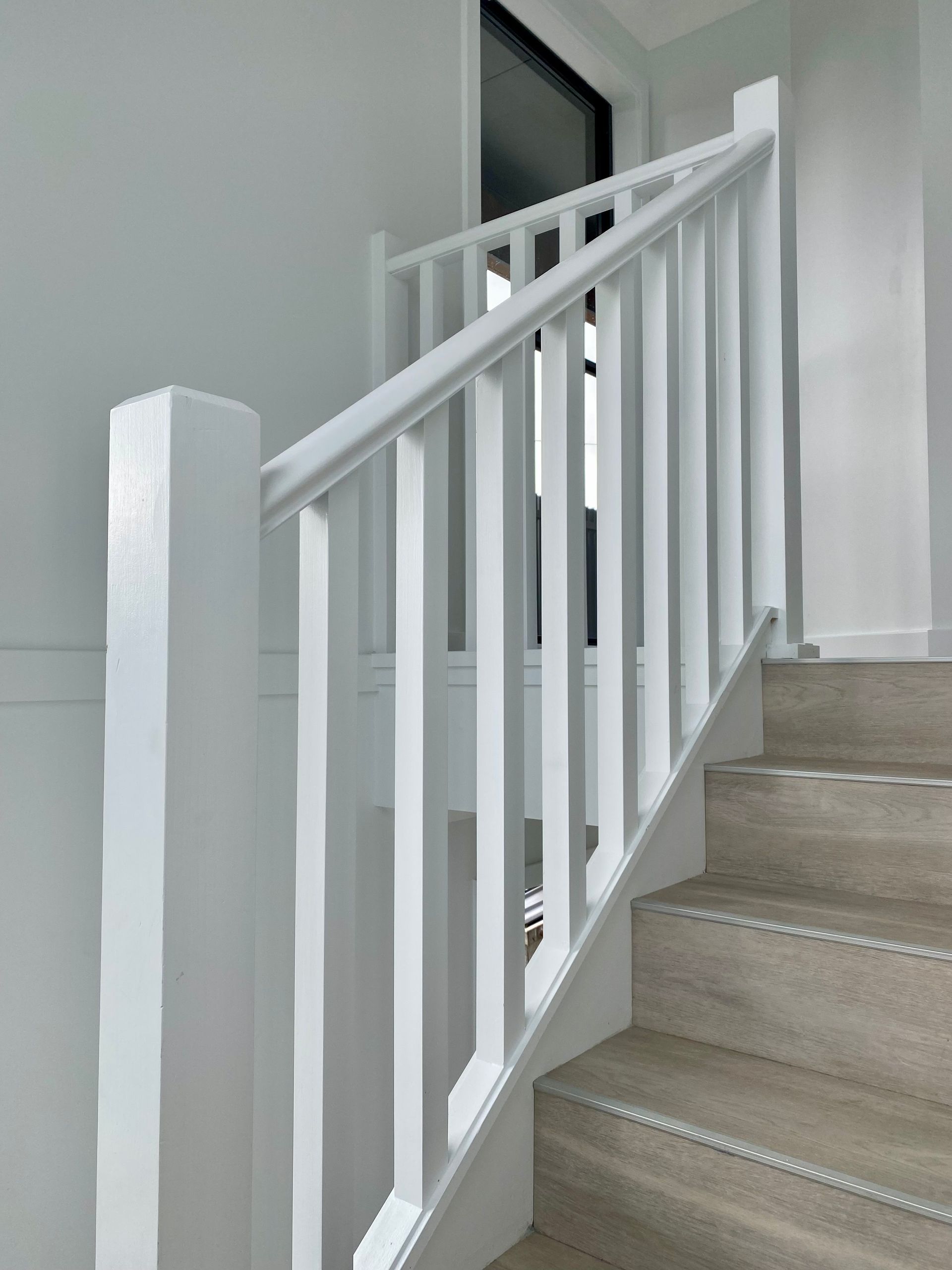 White staircase with banister and vertical slats, ascending toward a window.
