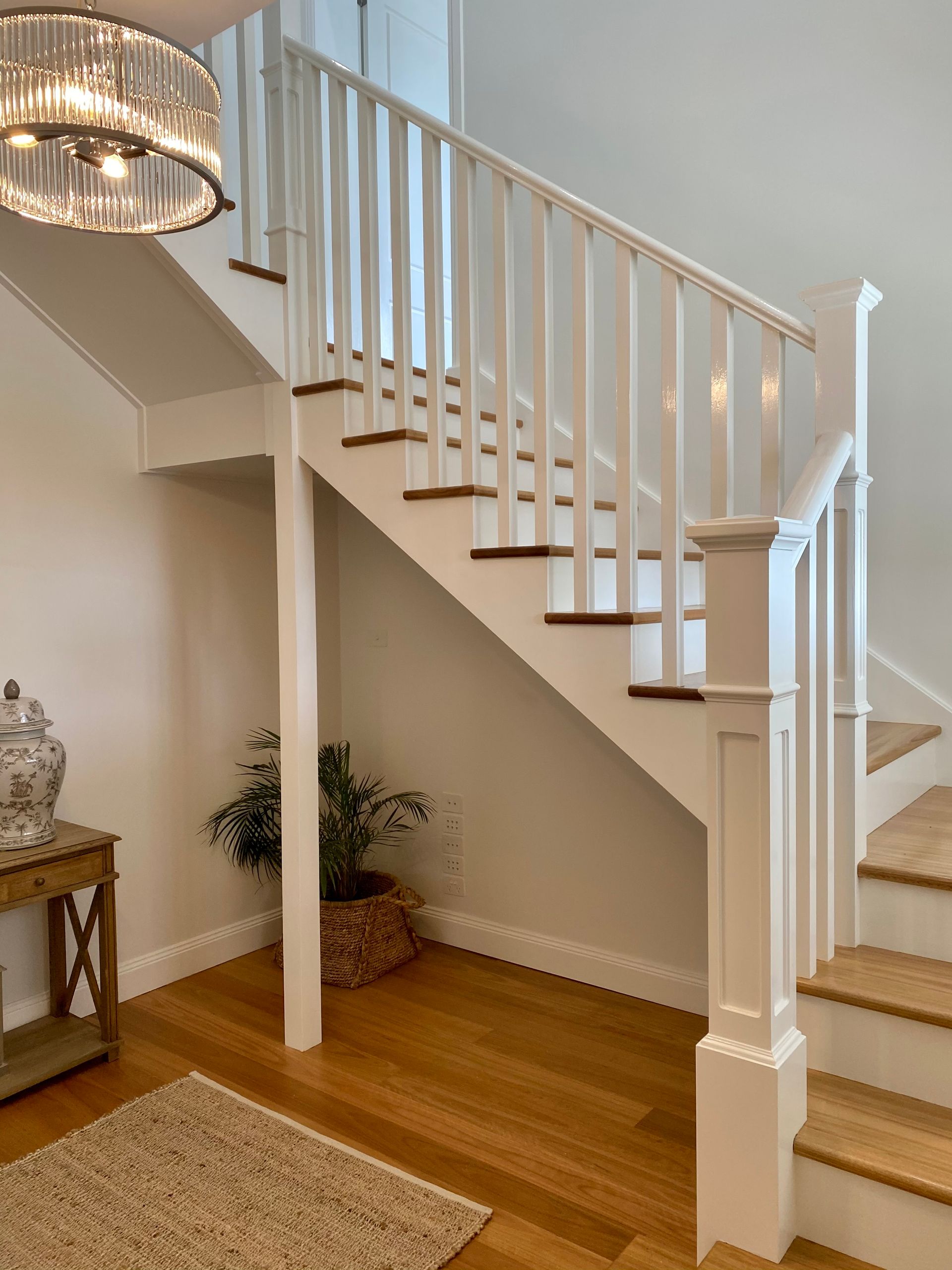 Wooden staircase with white banisters, wood floors, and a woven basket with a plant.