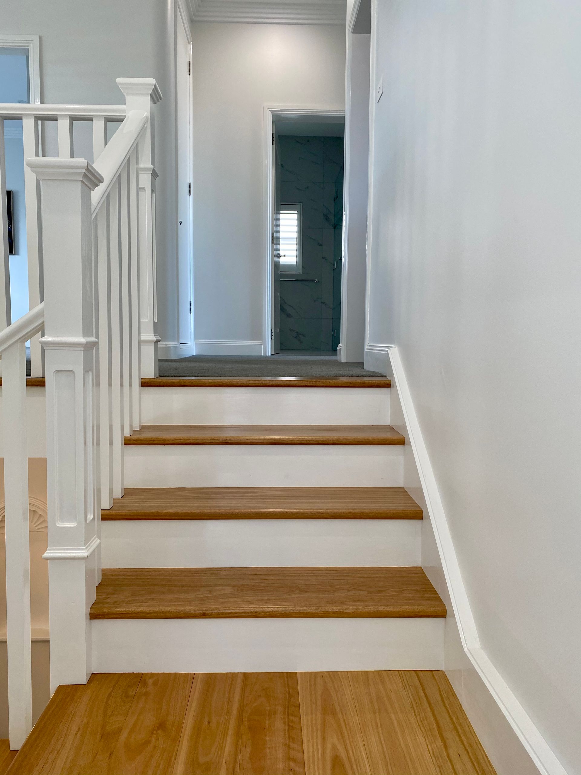Wooden staircase with white railings and walls leading to a hallway with a doorway.