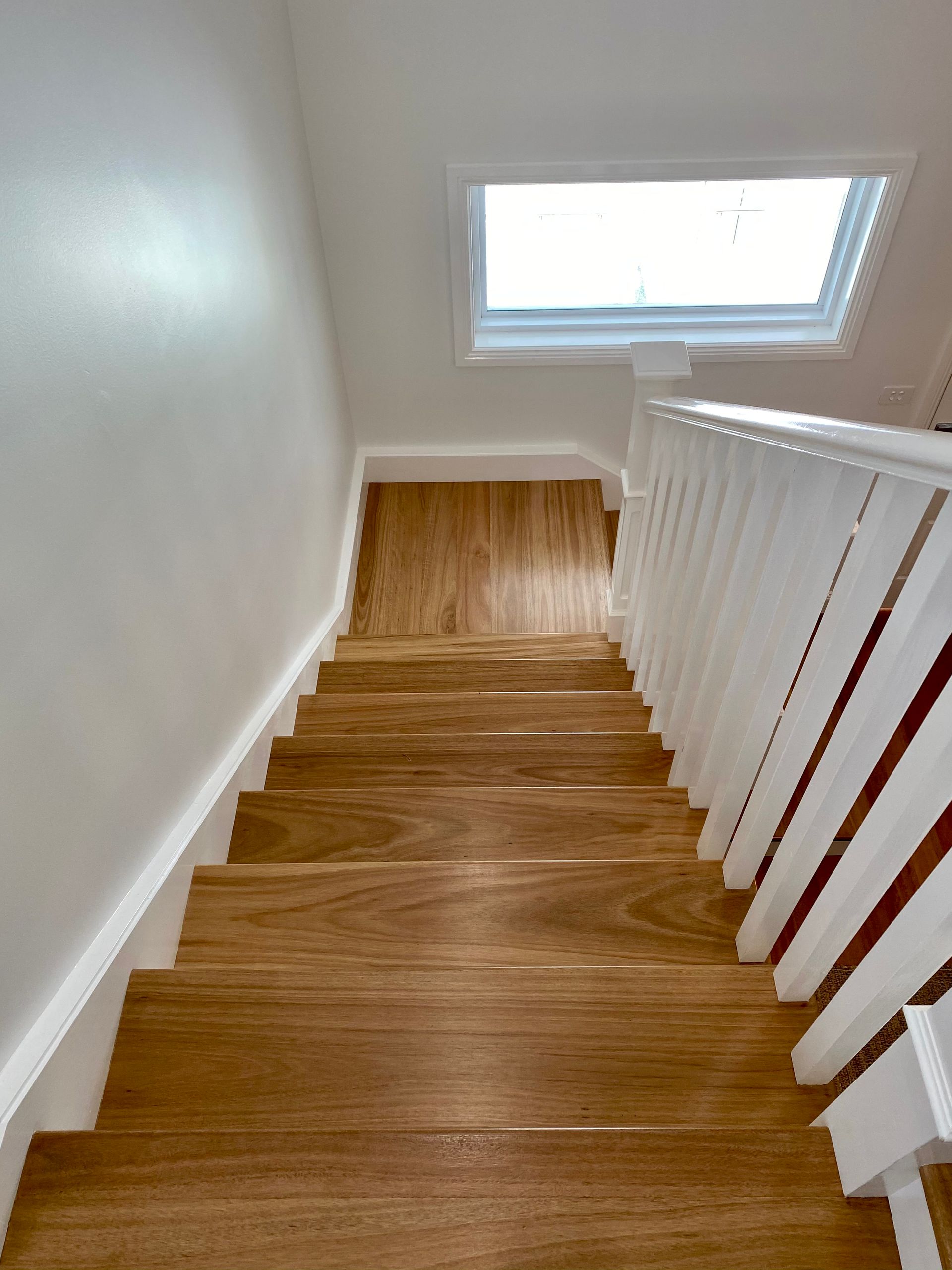 Wooden staircase with white railing leading down, bathed in sunlight.