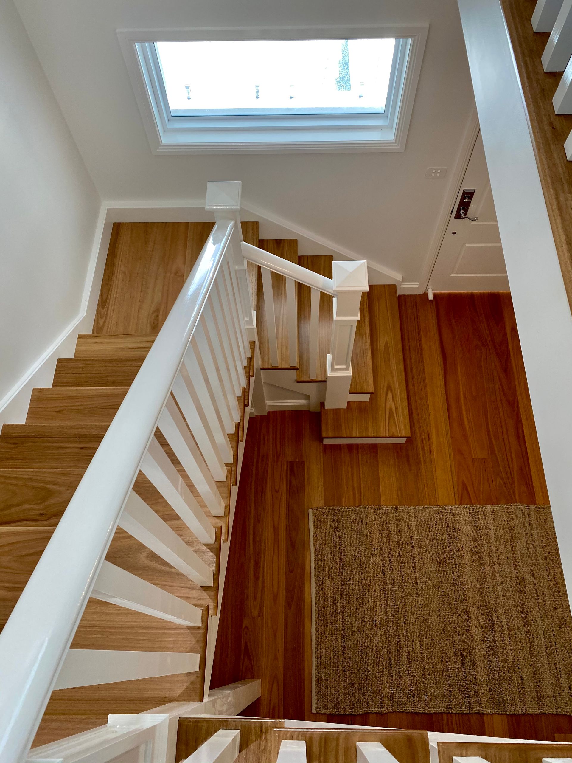 Wooden staircase with white railing and skylight above.