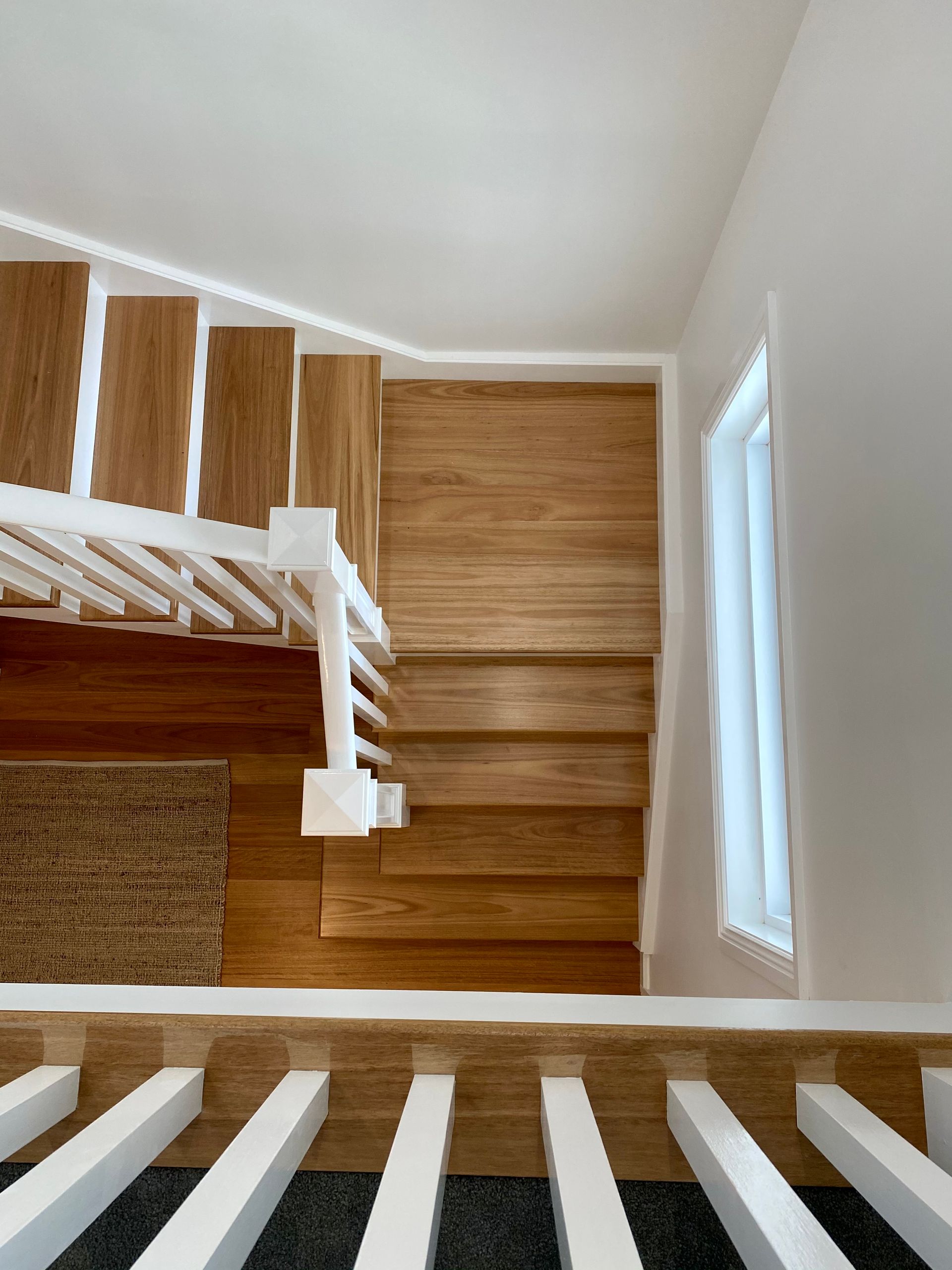 Wooden stairs with white railing, viewed from above.