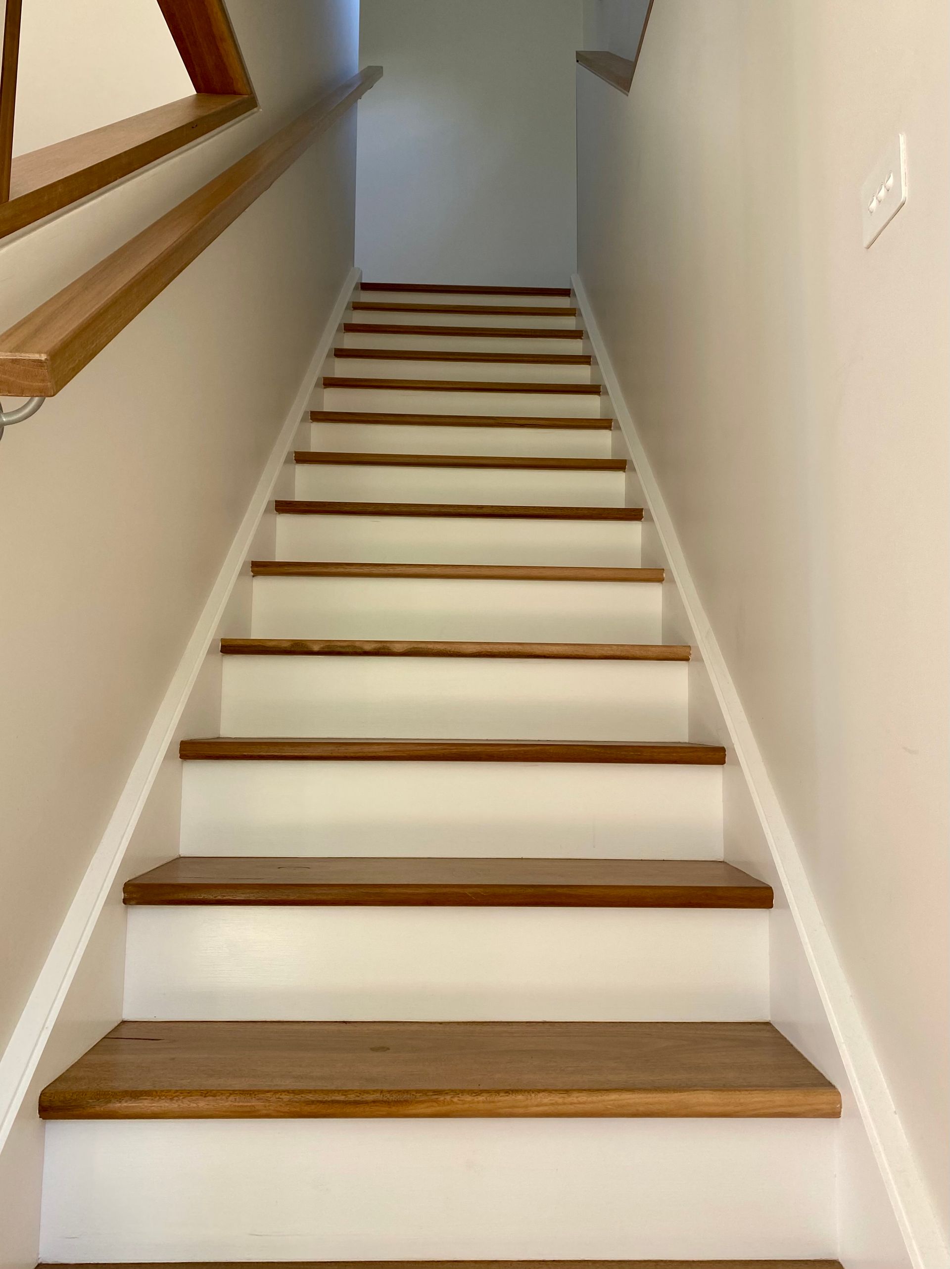 Wooden stairs with white risers and a wood handrail lead up a neutral wall.