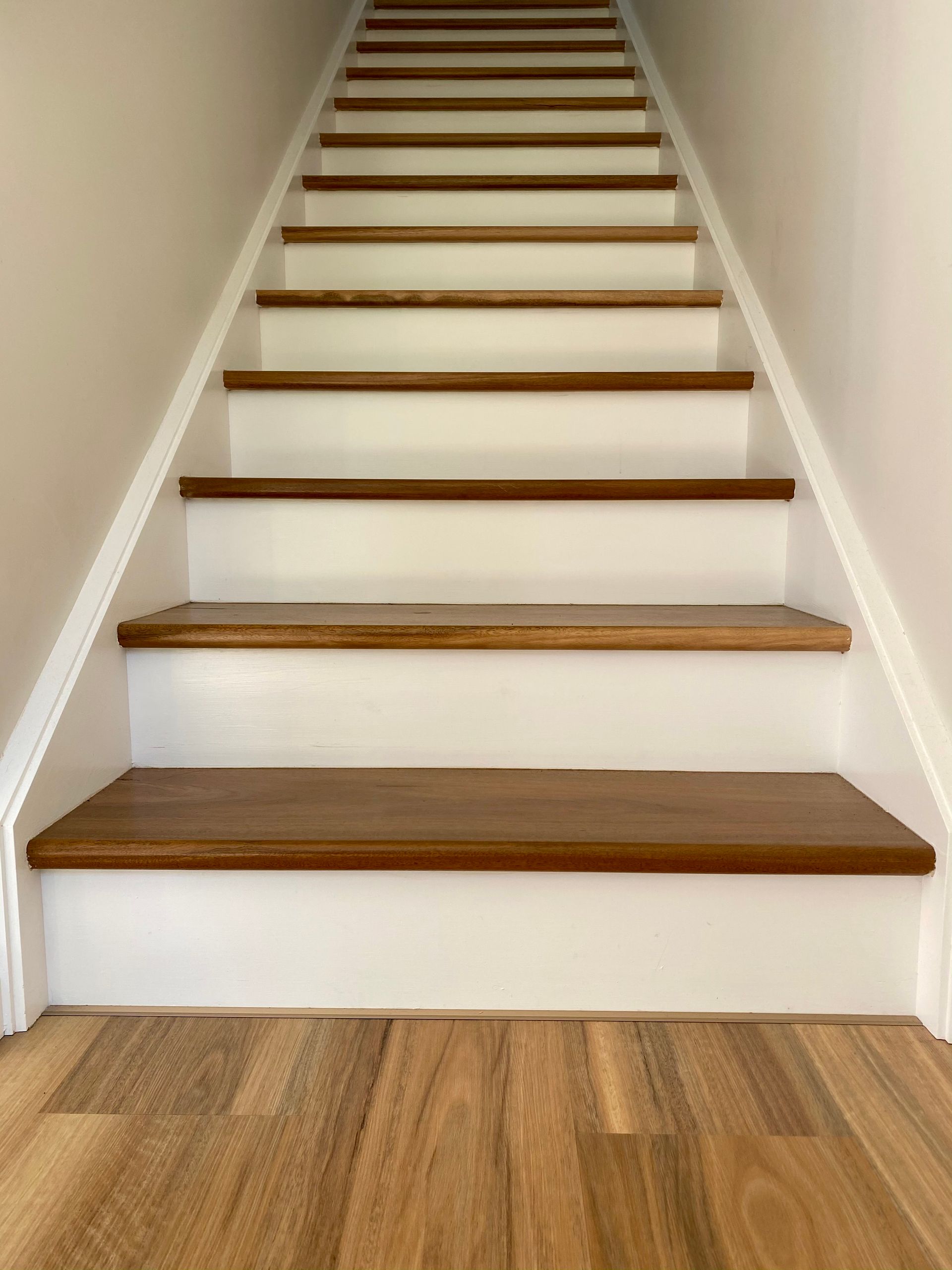 Wooden staircase with brown treads, white risers, and beige walls.