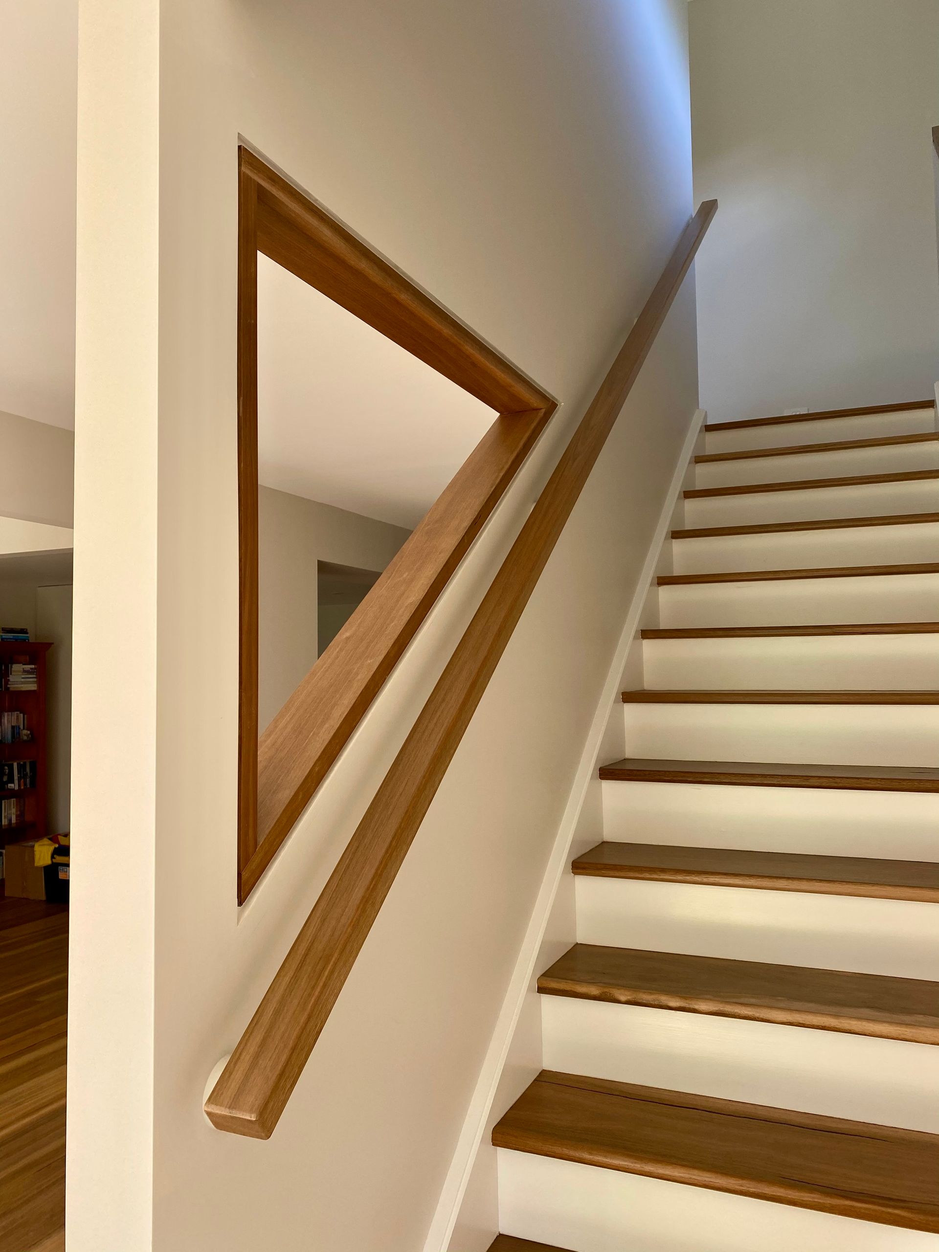 Wooden staircase with a diagonal handrail and a triangular mirror.